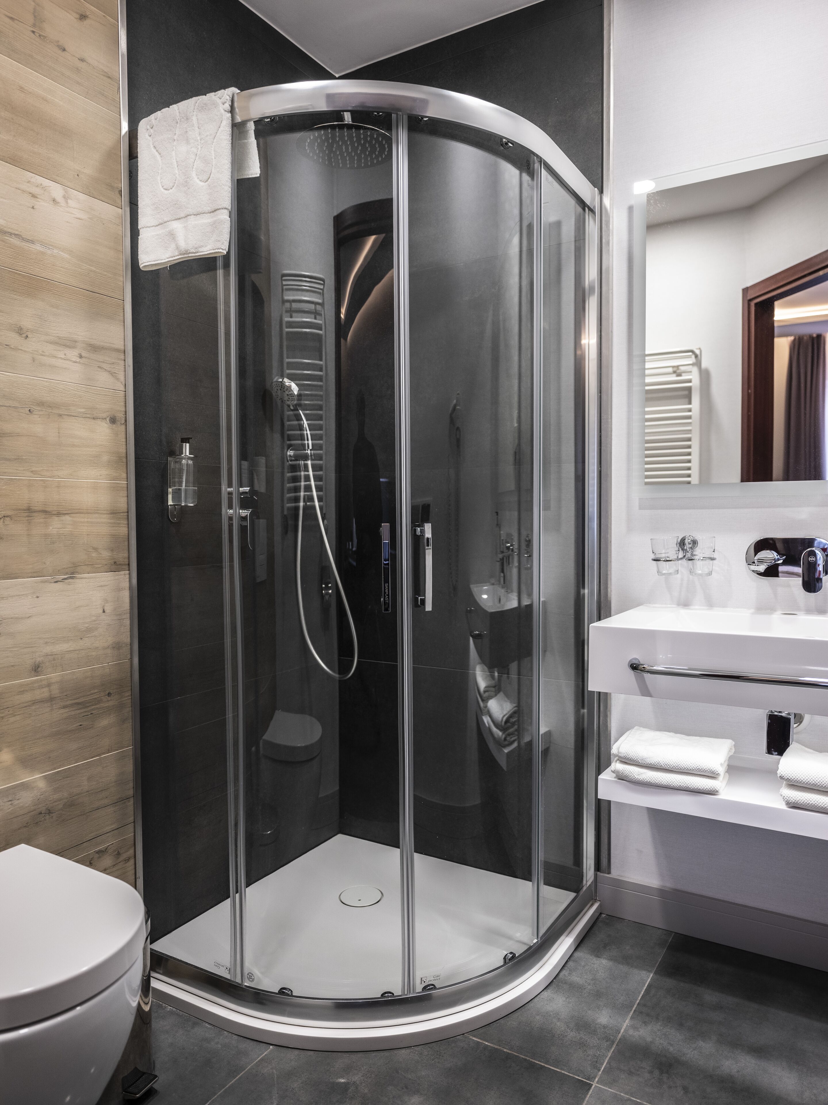 A modern bathroom with a glass-enclosed shower, a white toilet, and a vanity with a mirror.