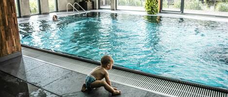 Una piscina interior con un niño sentado en el borde.
