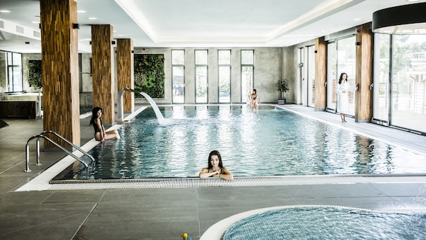Une piscine intérieure dotée de piliers en bois, de murs en verre transparent et d’un sol carrelé.