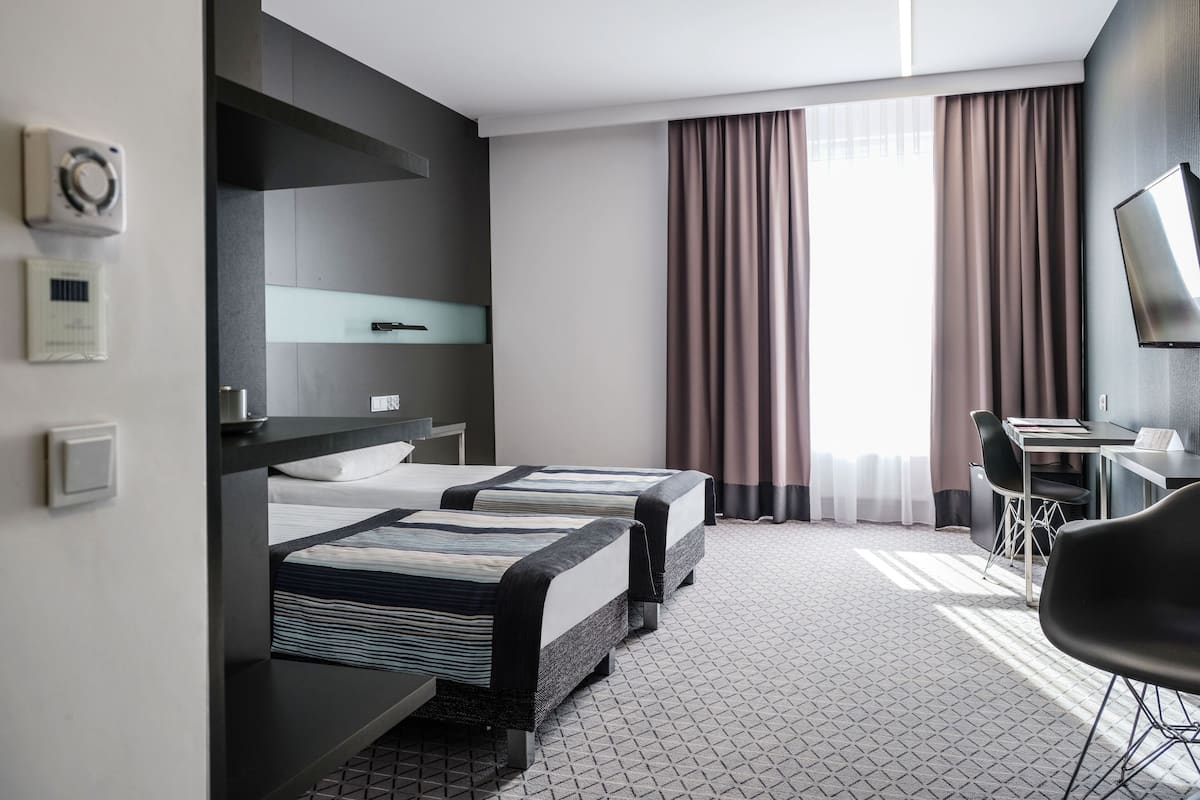 Een hotelkamer met twee bedden, een bureau, een stoel, een televisie en een raam met gordijnen.