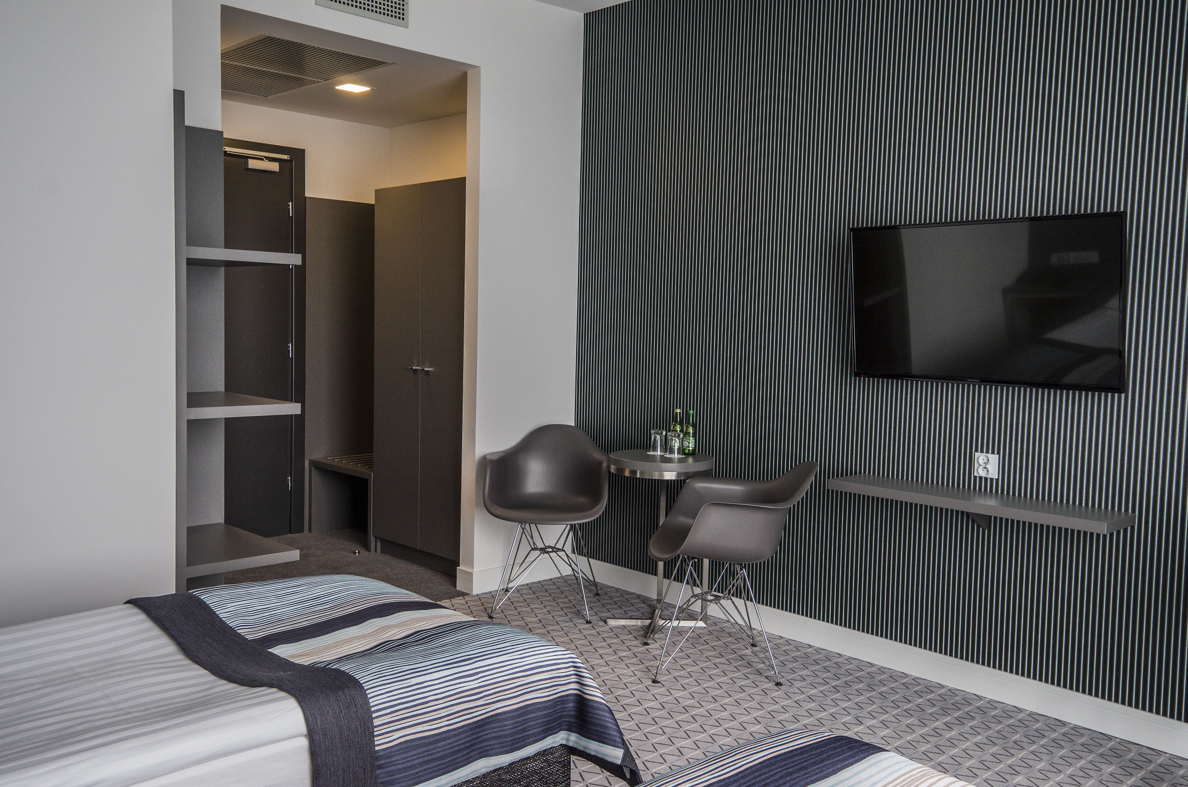 Habitación de hotel con cama, escritorio con dos sillas, televisor y armarios empotrados.