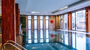 A large indoor swimming pool with clear glass walls, wooden paneling, and a lifebuoy on the wall.