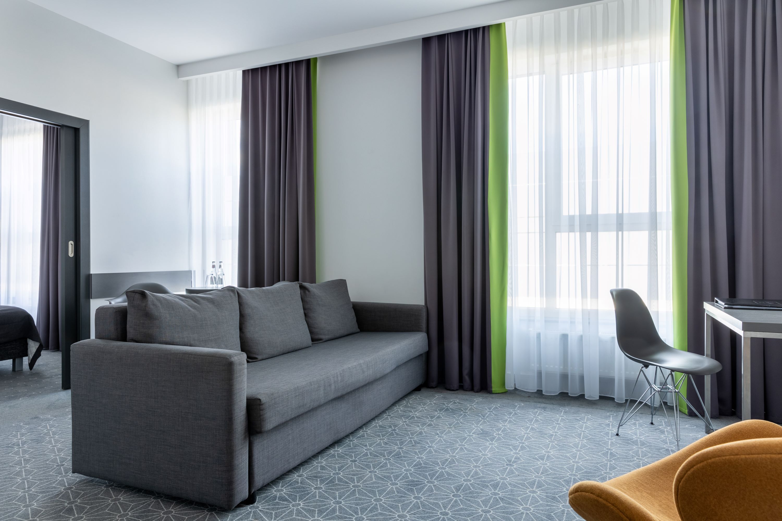Una habitación de hotel moderna con un sofá gris, una sola silla y una pequeña mesa.