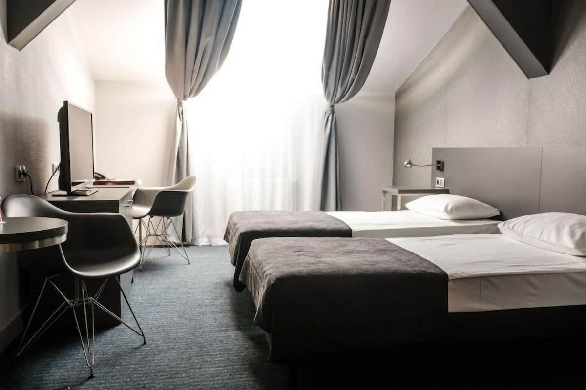 Een hotelkamer met twee bedden, een bureau met een computer, een stoel en een kleine tafel.