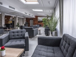 Uma área de estar moderna com assentos estofados em cinza, uma mesa de madeira e plantas em vasos.
