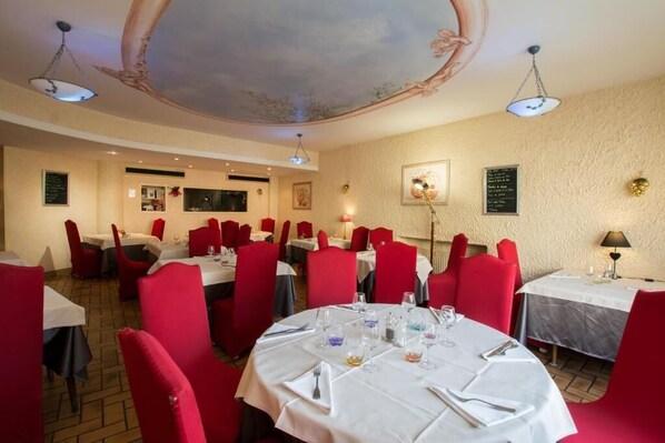 Un restaurante con mesas redondas, sillas rojas y un techo decorado con motivos florales.