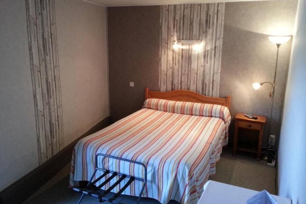 Een kleine, verzorgde slaapkamer met een enkel bed, een nachtkastje en een lamp.