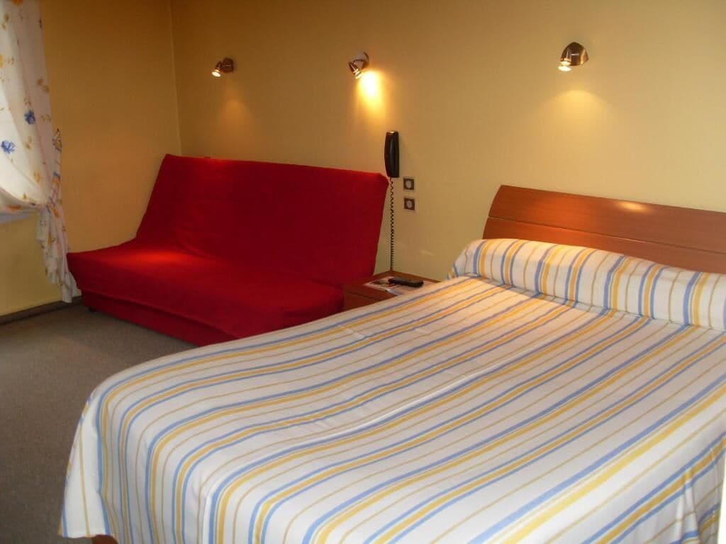 A hotel room with a bed, a red chair, and a bedside telephone.