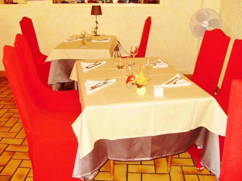 Ein Essbereich mit roten Stühlen und Tischen, jeweils gedeckt mit Besteck und Gläsern, und ein Ventilator an der Wand.