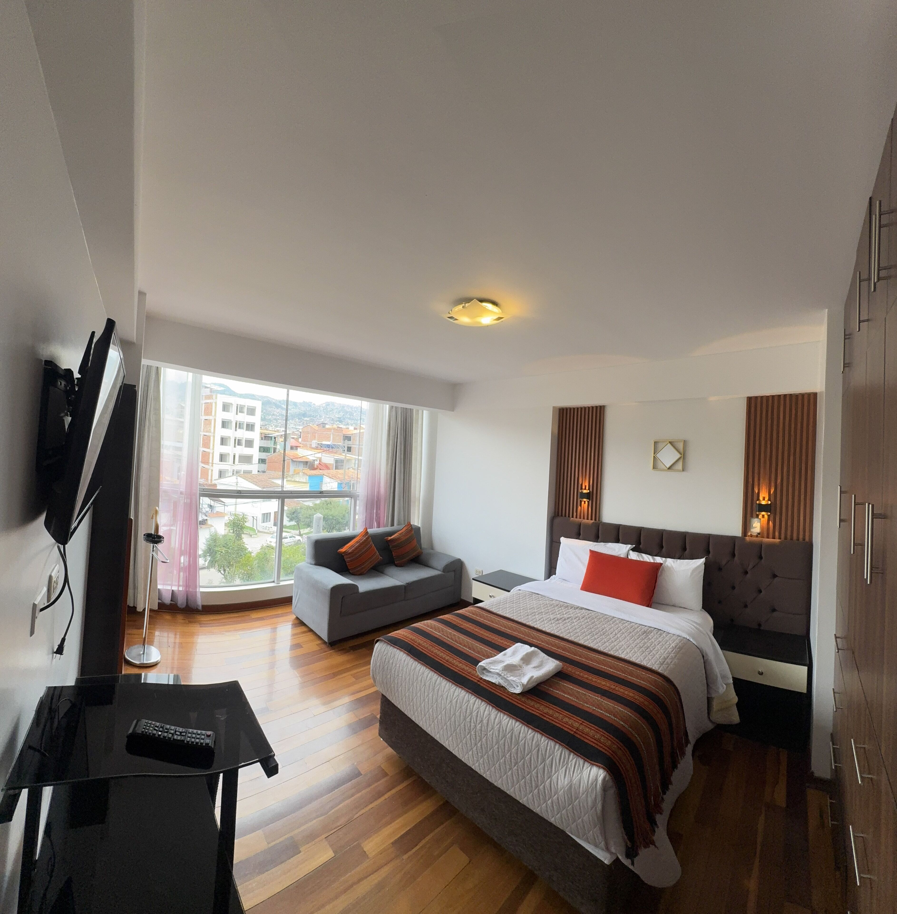 A modern hotel room with a large bed, a sofa, a TV, and a view of the city.