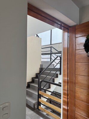 Una escalera con barandilla de madera y pasamanos de metal, que sube a un piso superior.