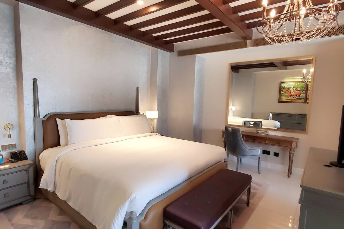 Et hotelværelse med seng, natbord, lampe, skrivebord med stol og et fjernsyn.