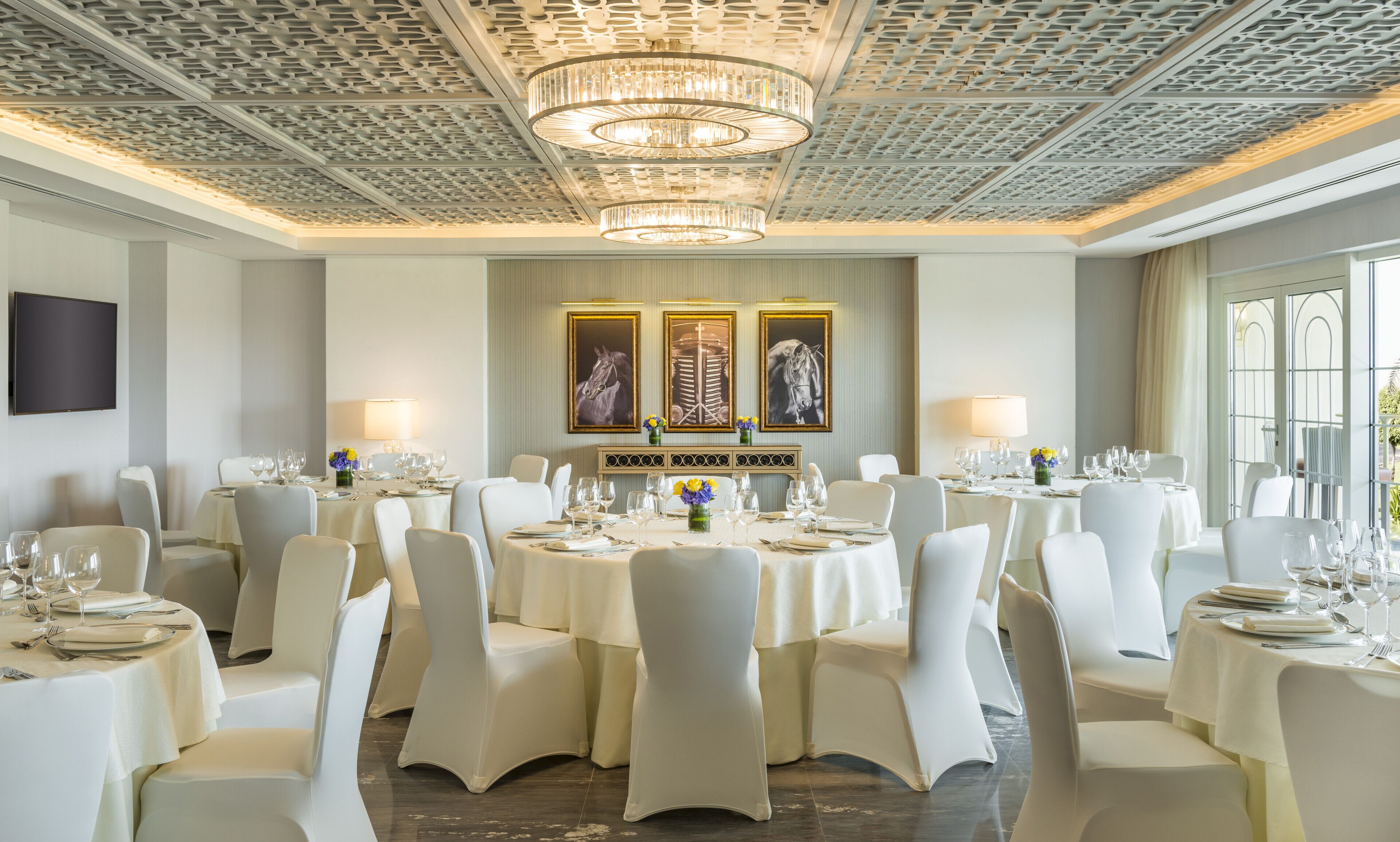 Un comedor elegante con mesas redondas, sillas blancas y candelabros.