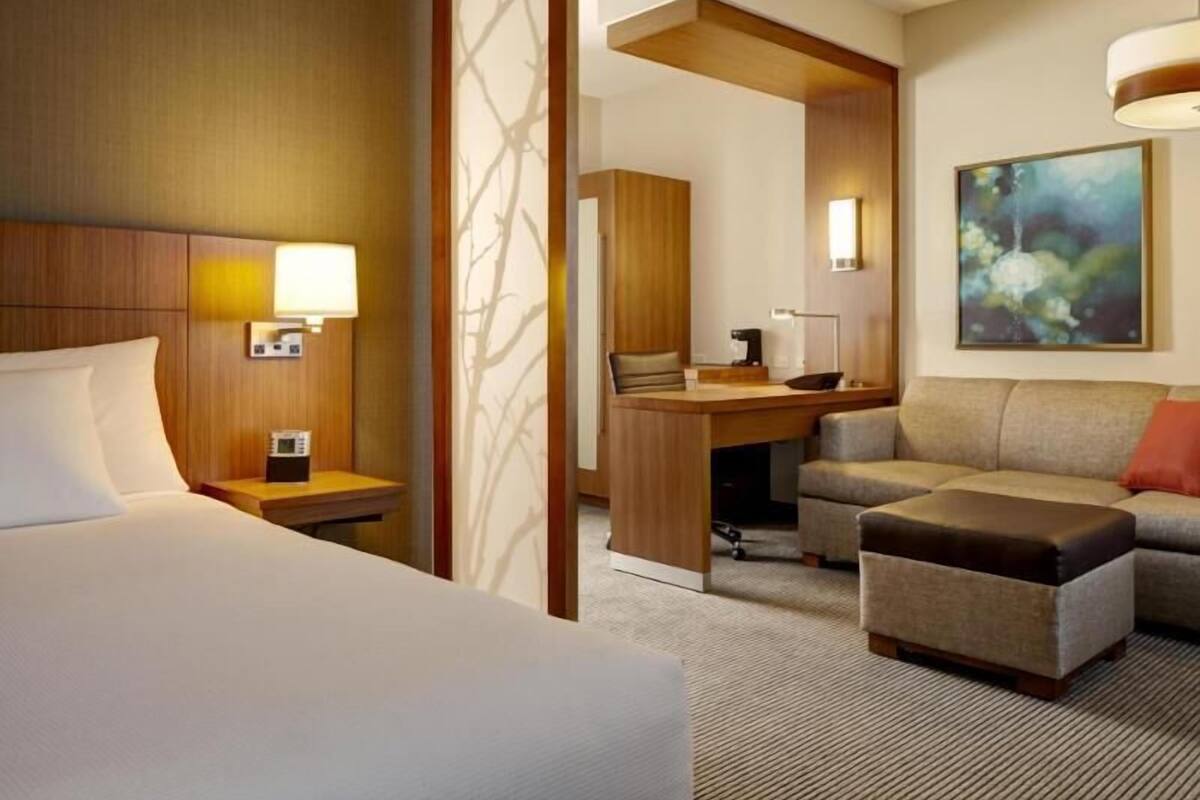 A hotel room with a bed, a desk, a sofa, and a painting on the wall.