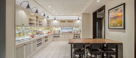 A modern kitchen with a dining area, featuring a long counter, built-in cabinets, and pendant lighting.