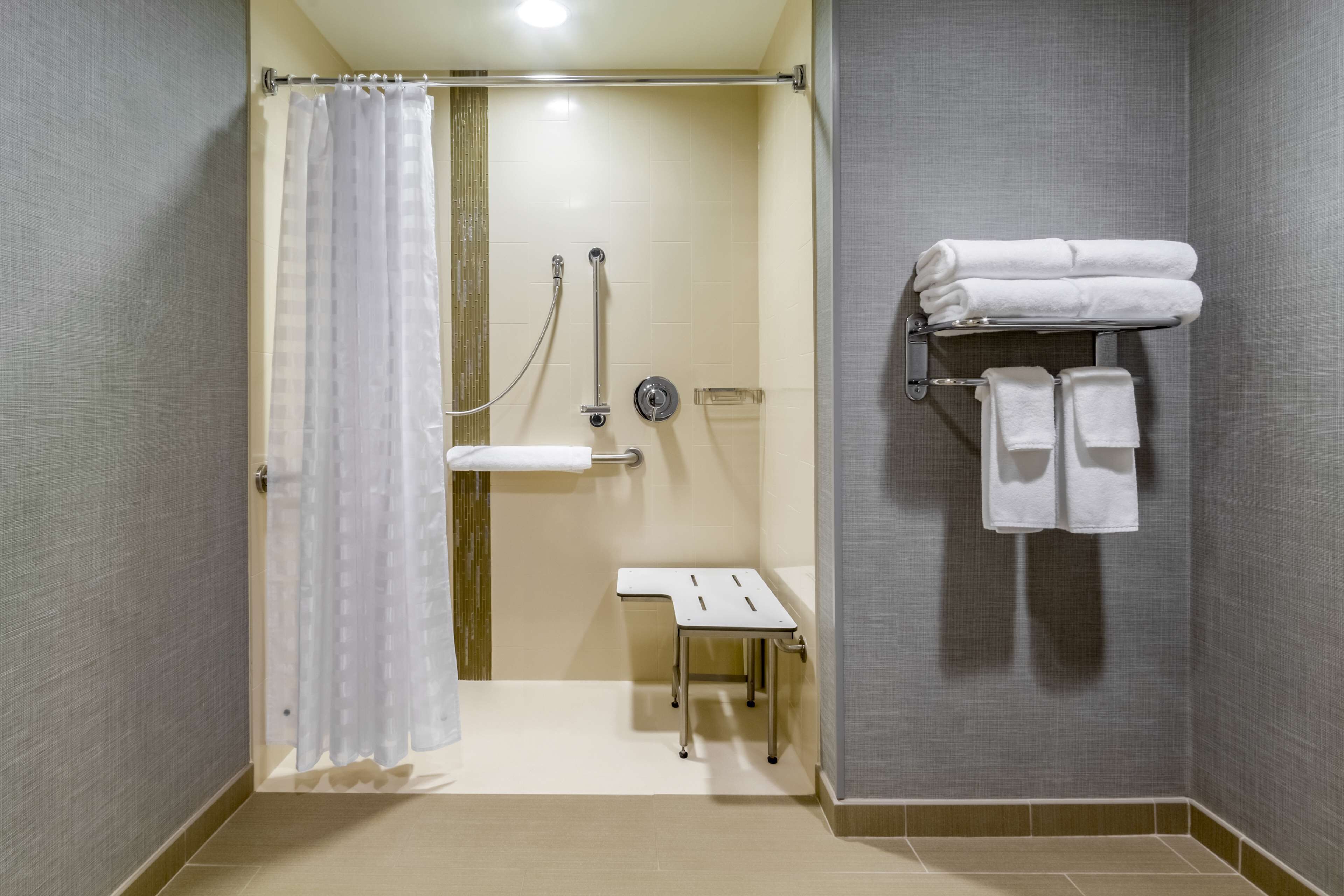 Un baño con ducha, una mesita y un perchero con toallas.