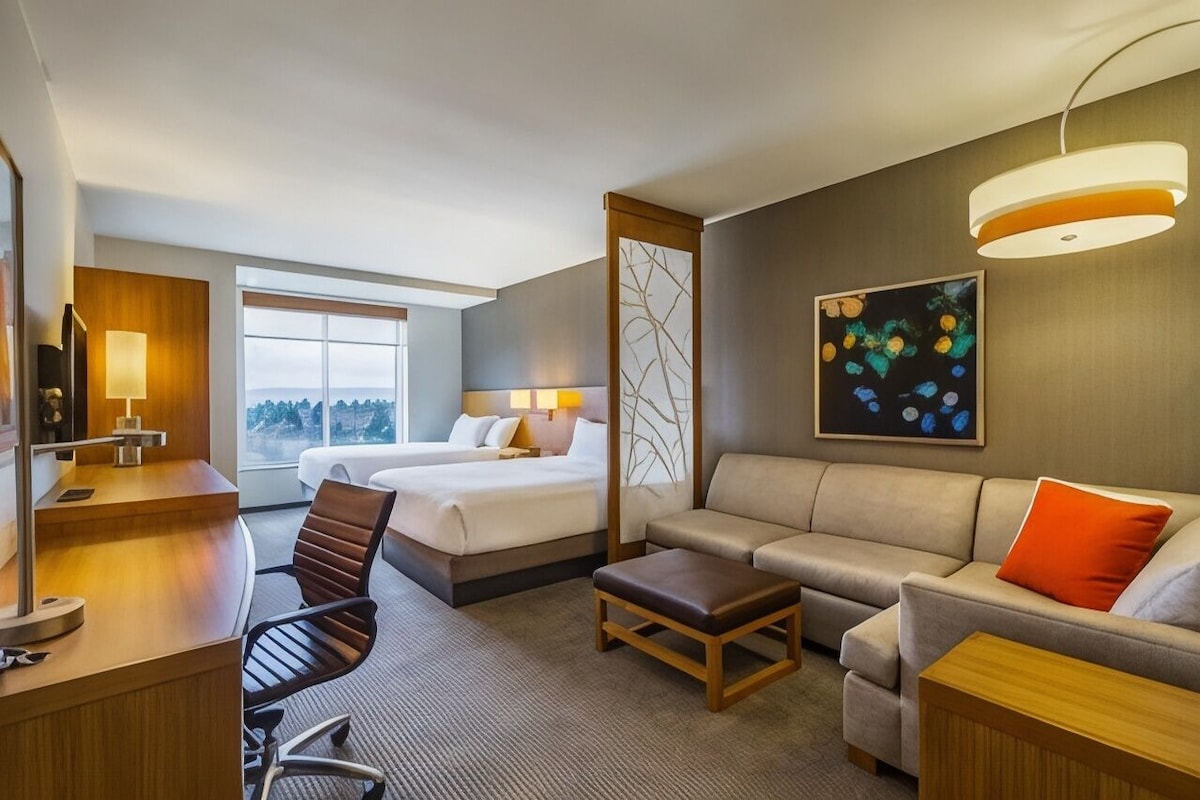 A hotel room with a bed, a sofa, a desk, a chair, a lamp, and a painting.