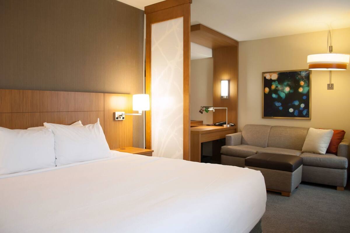A hotel room with a large bed, a desk with a chair, a sofa, and a painting on the wall.