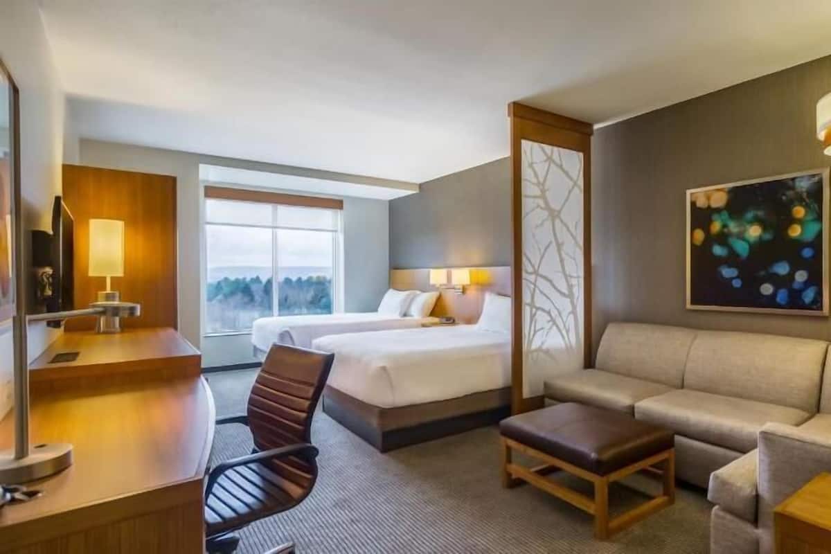 A hotel room with two beds, a sofa, a desk, and a chair.