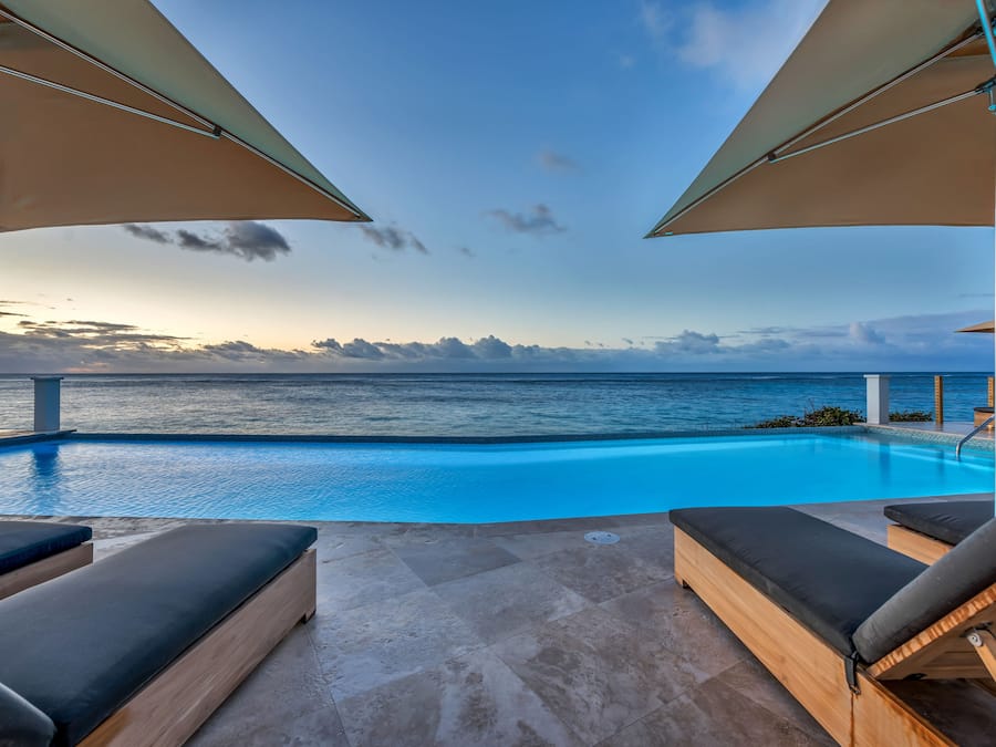 An infinity pool with a view of the ocean, surrounded by lounge chairs and umbrellas.