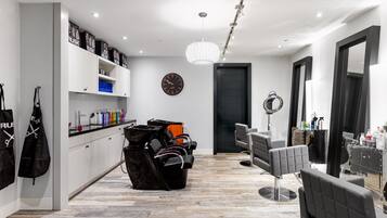 Un moderno salón de belleza con un diseño limpio y minimalista, que presenta un suelo de madera, muebles blancos y un espejo grande con luz de aro.