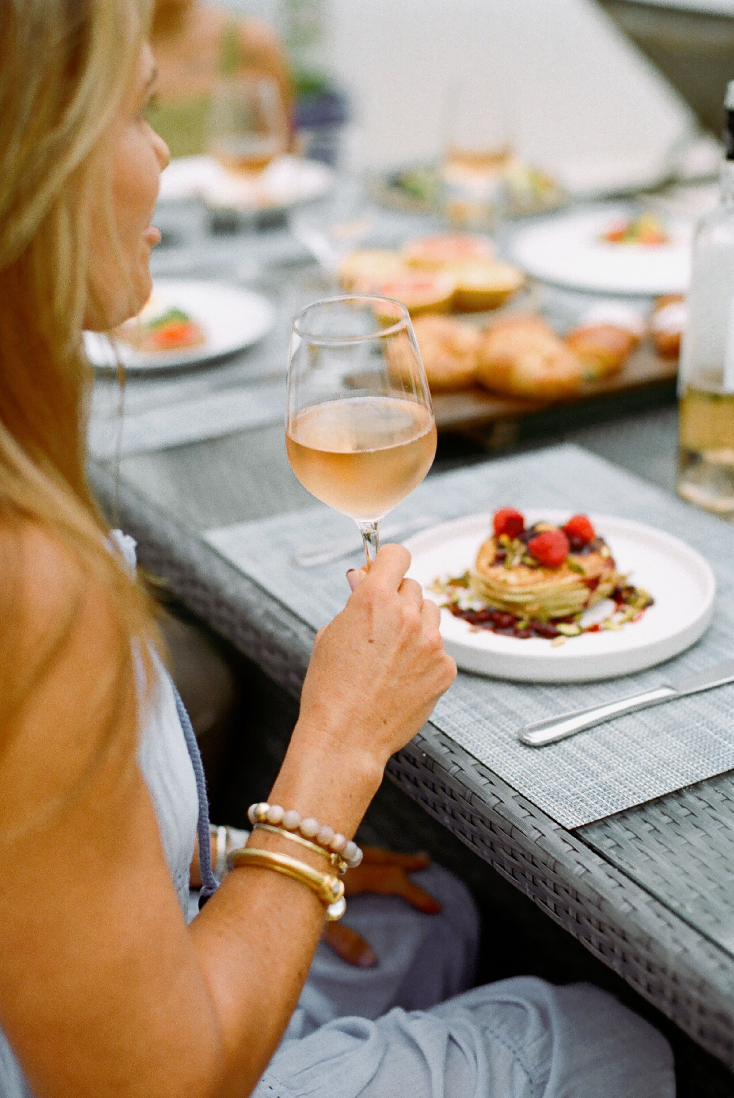 A person holding a glass of wine at a table with a plate of food and a bottle of water.