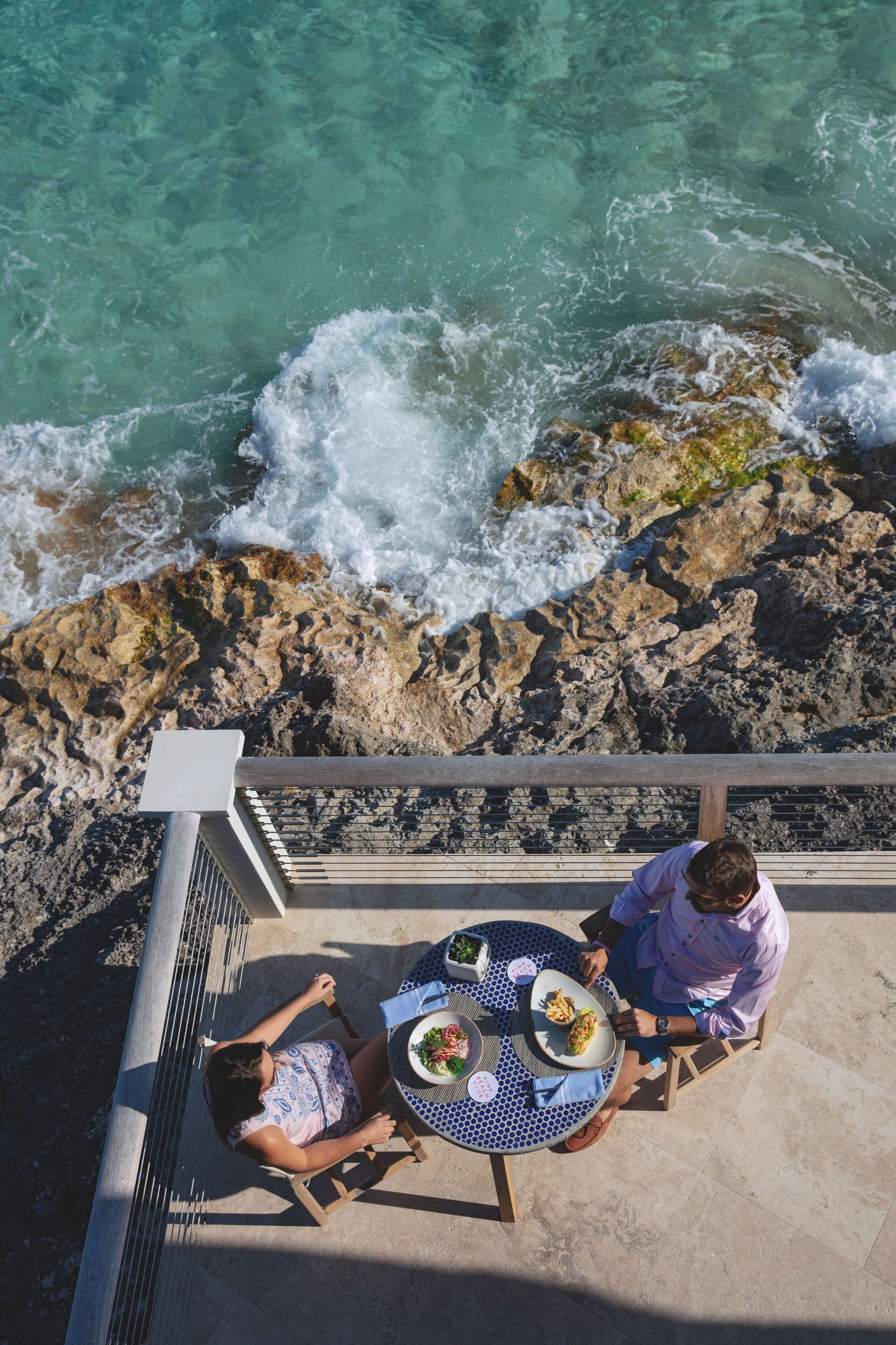 Un comedor con mesa y sillas con vista a un litoral rocoso donde las olas rompen contra las rocas.