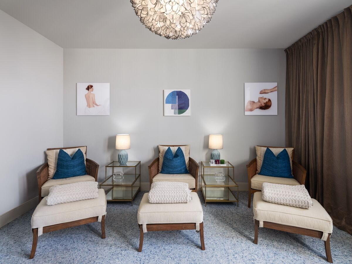 Una habitación moderna con tres sillones, una mesa redonda y un amplio ventanal con cortinas.