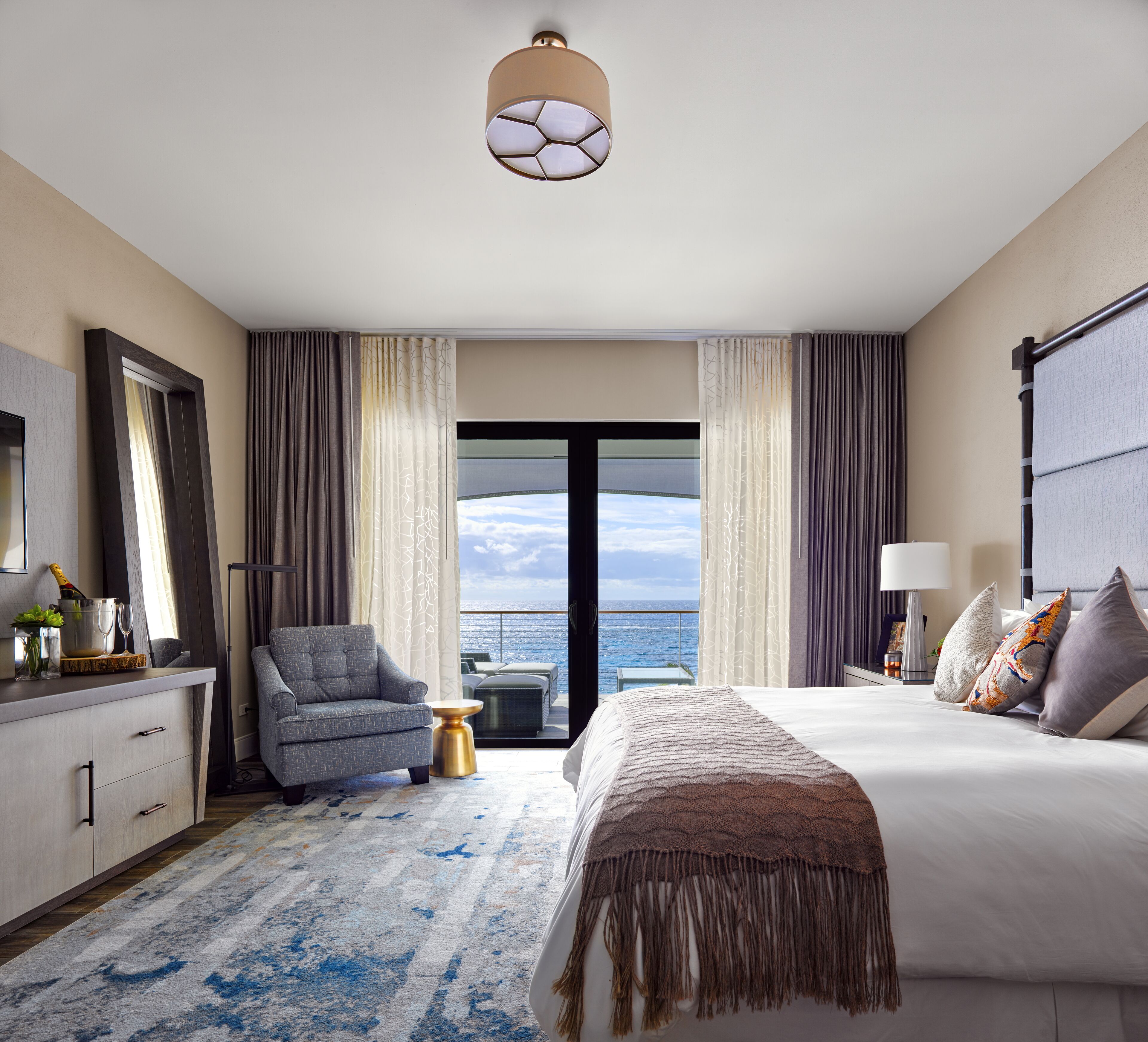 A modern hotel room with a large bed, a seating area, and a view of the ocean.