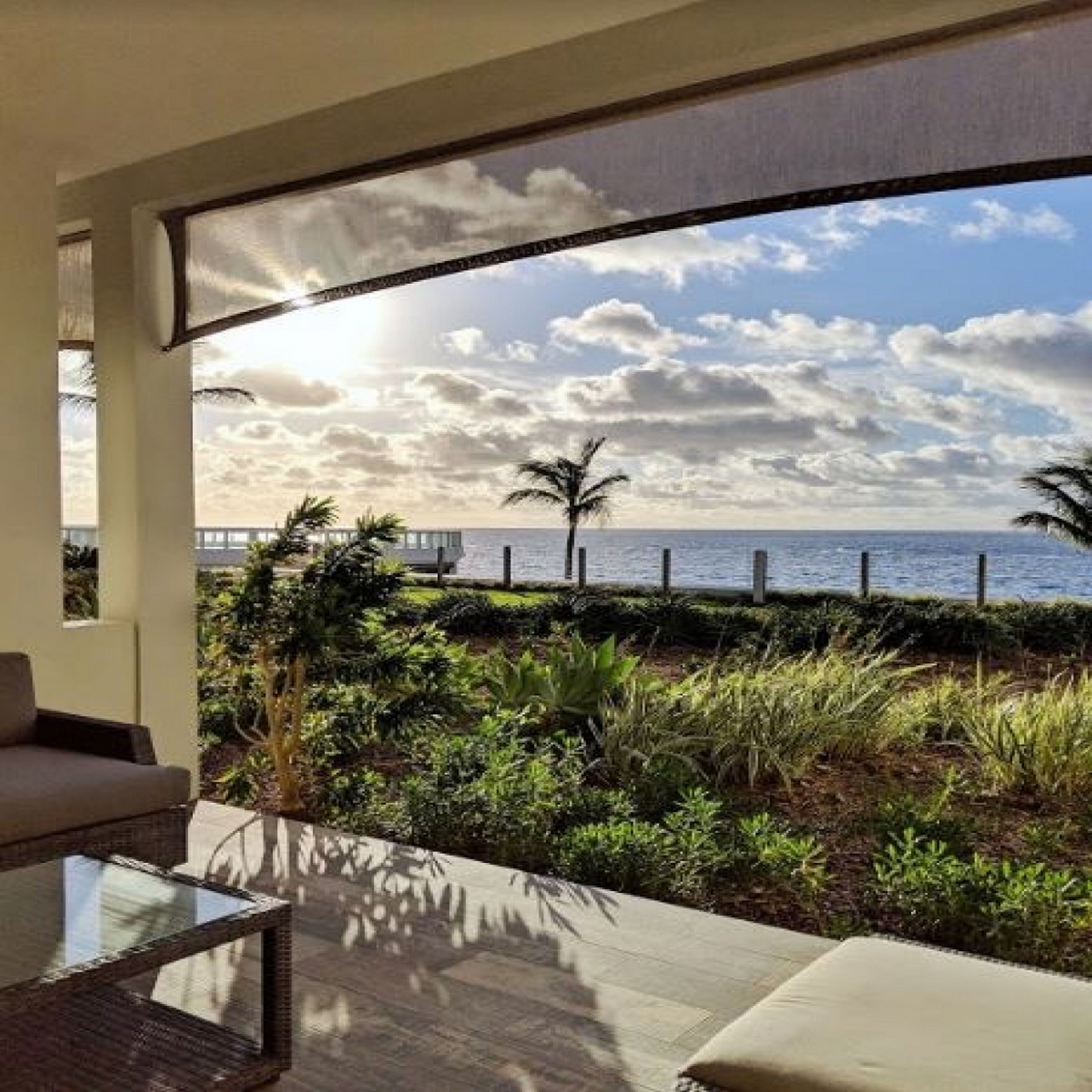 Ein moderner Sitzbereich im Freien mit Blick auf das Meer und Palmen.