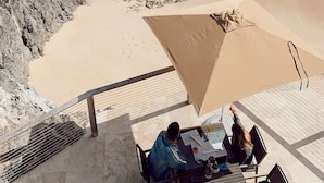 Vista frente a la playa con un área de comedor que da al océano, con mesas y sillas bajo una estructura cubierta.