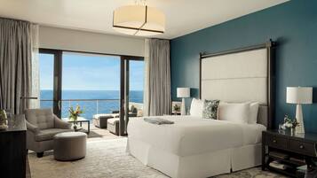 Quarto de hotel moderno com uma cama grande, área de estar, varanda vista para o mar e uma janela ampla.