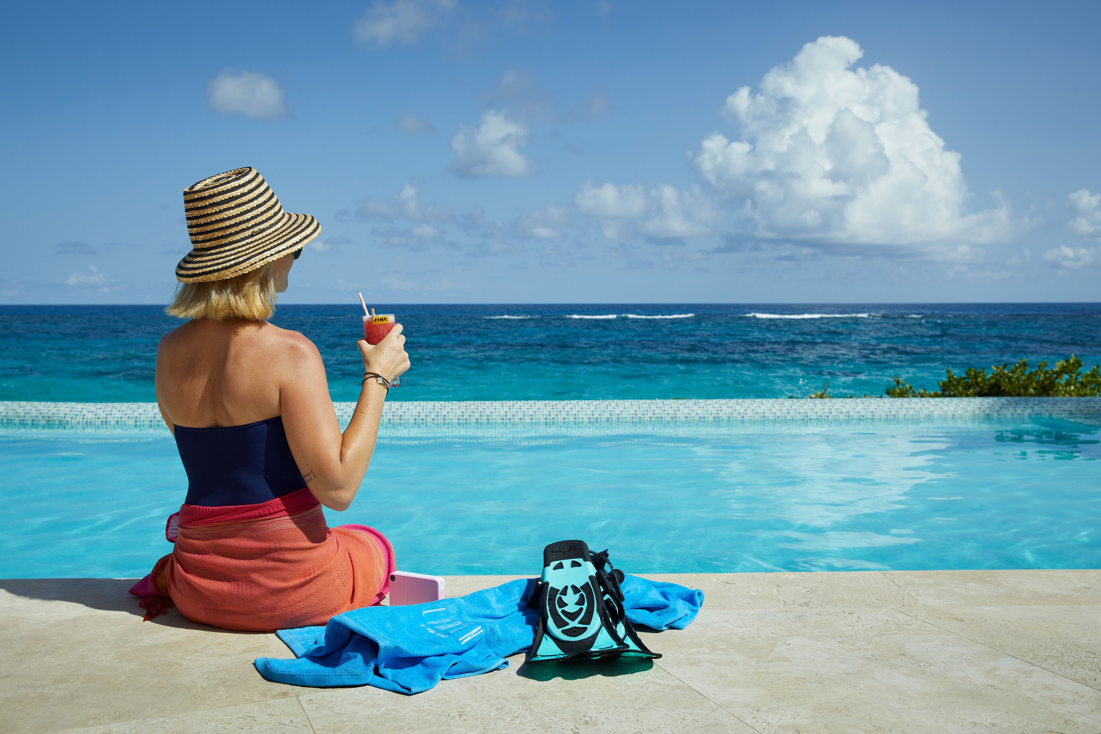 Eine Person sitzt am Pool mit Blick auf den Ozean.