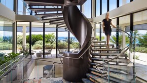 Una escalera espiral moderna con barandillas de vidrio, que conduce a un espacio exterior con asientos y plantas.