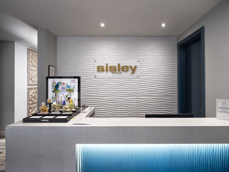 Een receptiebalie met een Sisley Paris logo, een digitaal scherm dat een bloemendessin toont, en een bord met daop de tekst 'spa'.