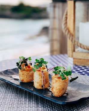 Tres aperitivos sobre un plato oscuro, colocados sobre un tapete tejido.
