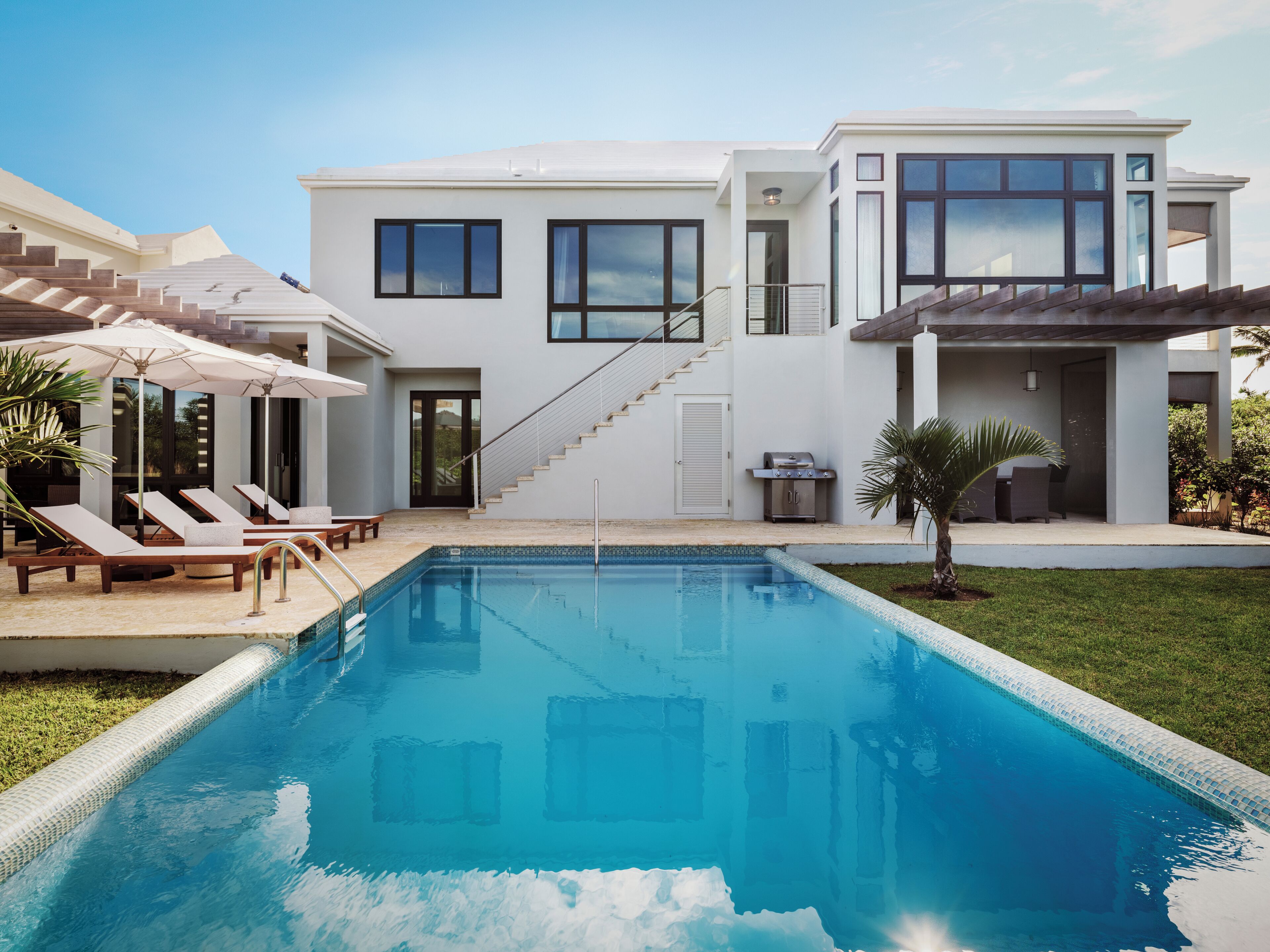 Una casa moderna con piscina, un porche cubierto con sillones de descanso y una escalera que lleva a la entrada principal.