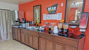 Ein Frühstücksbuffet mit einem Schild, das "BEAR Bites by Tracloche" zeigt, einer Kaffeemaschine, einer Obstschale und einem Saftspender.