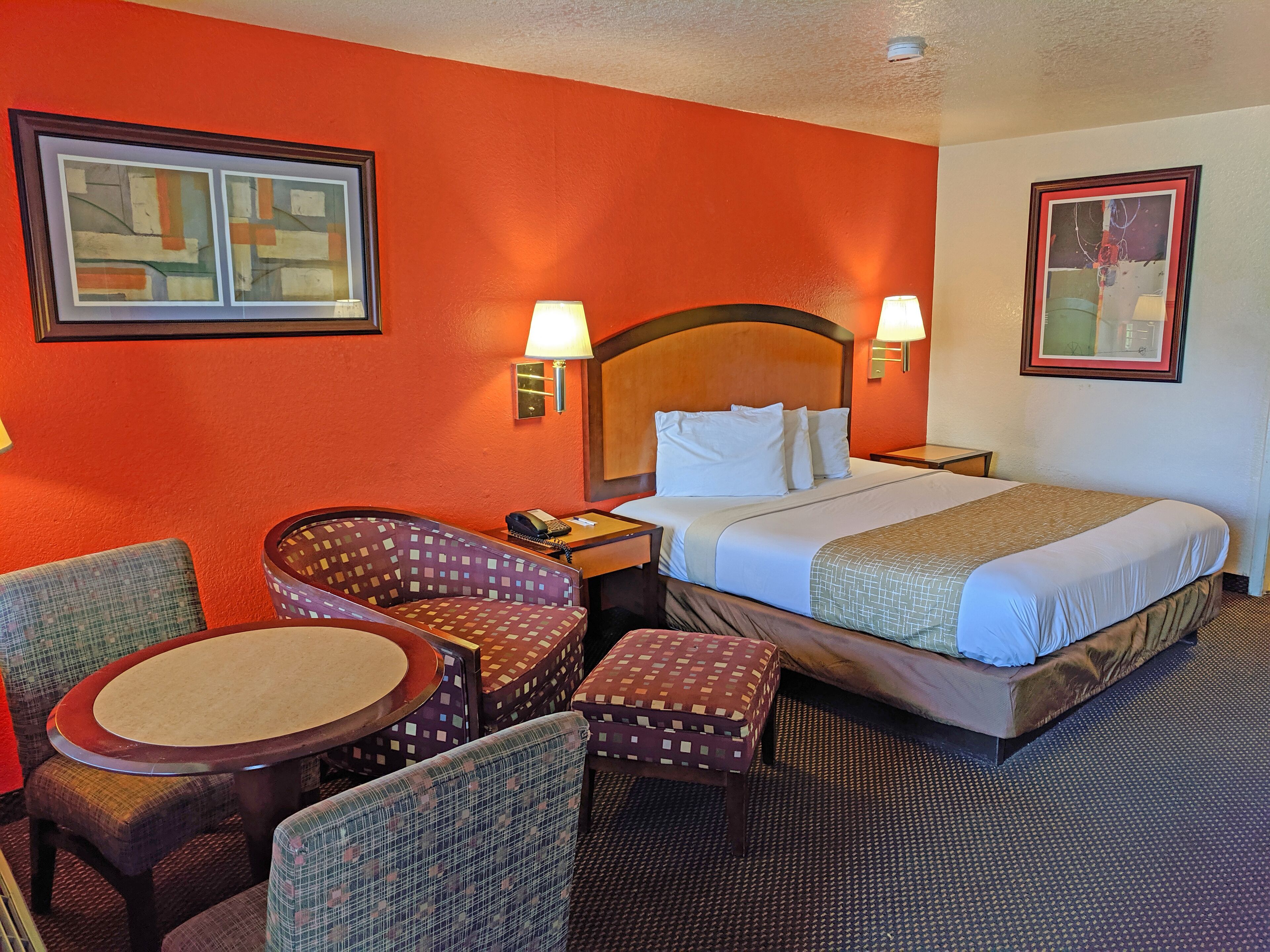 A hotel room with a large bed, two bedside lamps, a chair, a small table, and two framed pictures on the walls.
