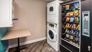 Ein Waschraum mit Waschmaschine, Trockner und einem Verkaufsautomaten für Snacks.