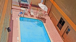 Ein rechteckiger Pool mit einem Sprungverbotsschild, umgeben von roter Ziegelstein-Bodenfliese, ausgestattet mit Liegestühlen und Sonnenschirmen.