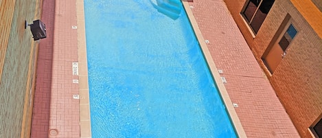 A rectangular pool with a no diving sign, surrounded by red brick flooring, and equipped with lounge chairs and umbrellas.
