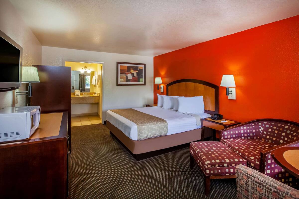 Ein Hotelzimmer mit einem Bett, einem Schreibtisch mit Mikrowelle, einem Sessel, einem kleinen Tisch und einer Wandleuchte.