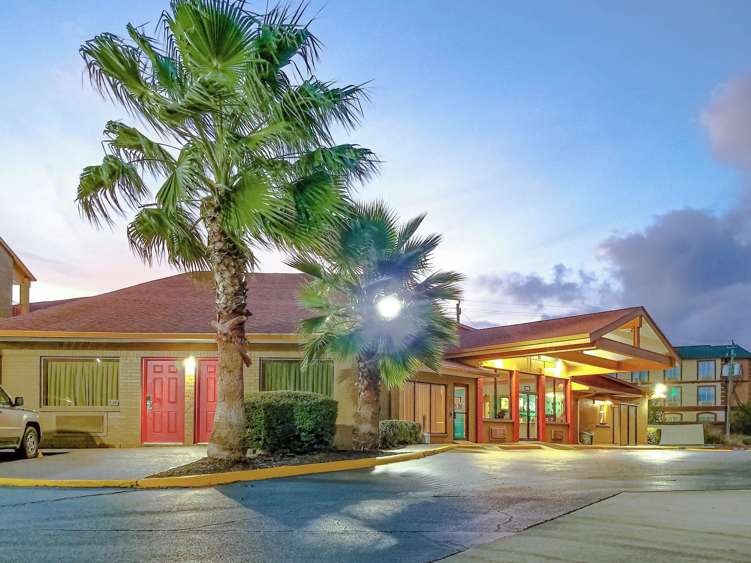 A hotel with a red door, palm trees, and a well-lit entrance.