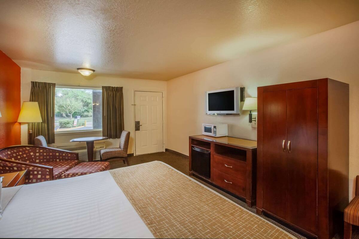 Ein Hotelzimmer mit einem Bett, einem Schreibtisch, einem Fernseher, einem Kleiderschrank und einem Vorhangfenster.