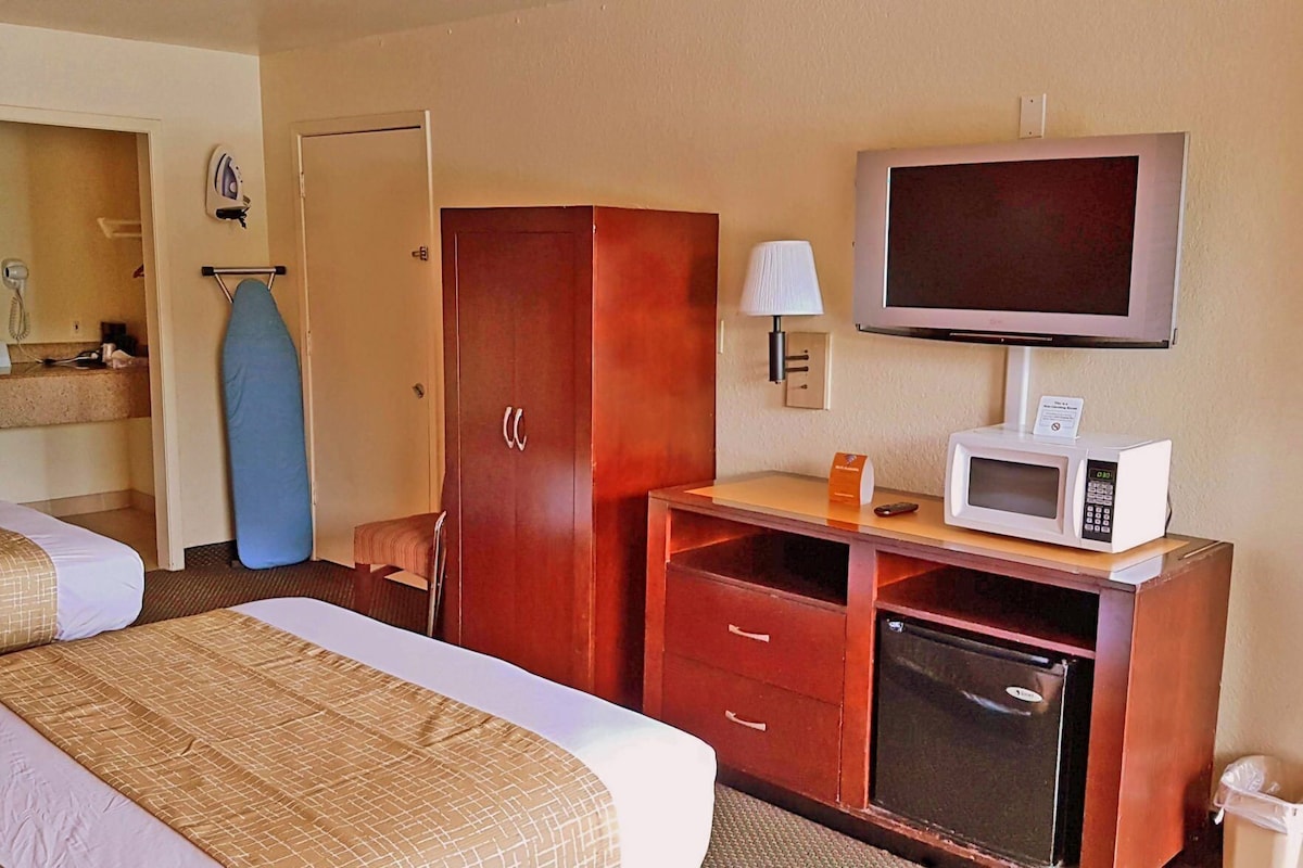 A hotel room with a bed, a wardrobe, a microwave, a television, and a small refrigerator.