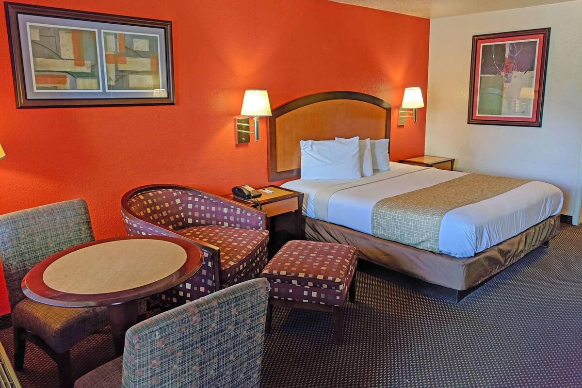 Ein Hotelzimmer mit einem Bett, zwei Nachttischlampen, einem Sessel, einem kleinen Tisch und zwei gerahmten Bildern an den Wänden.