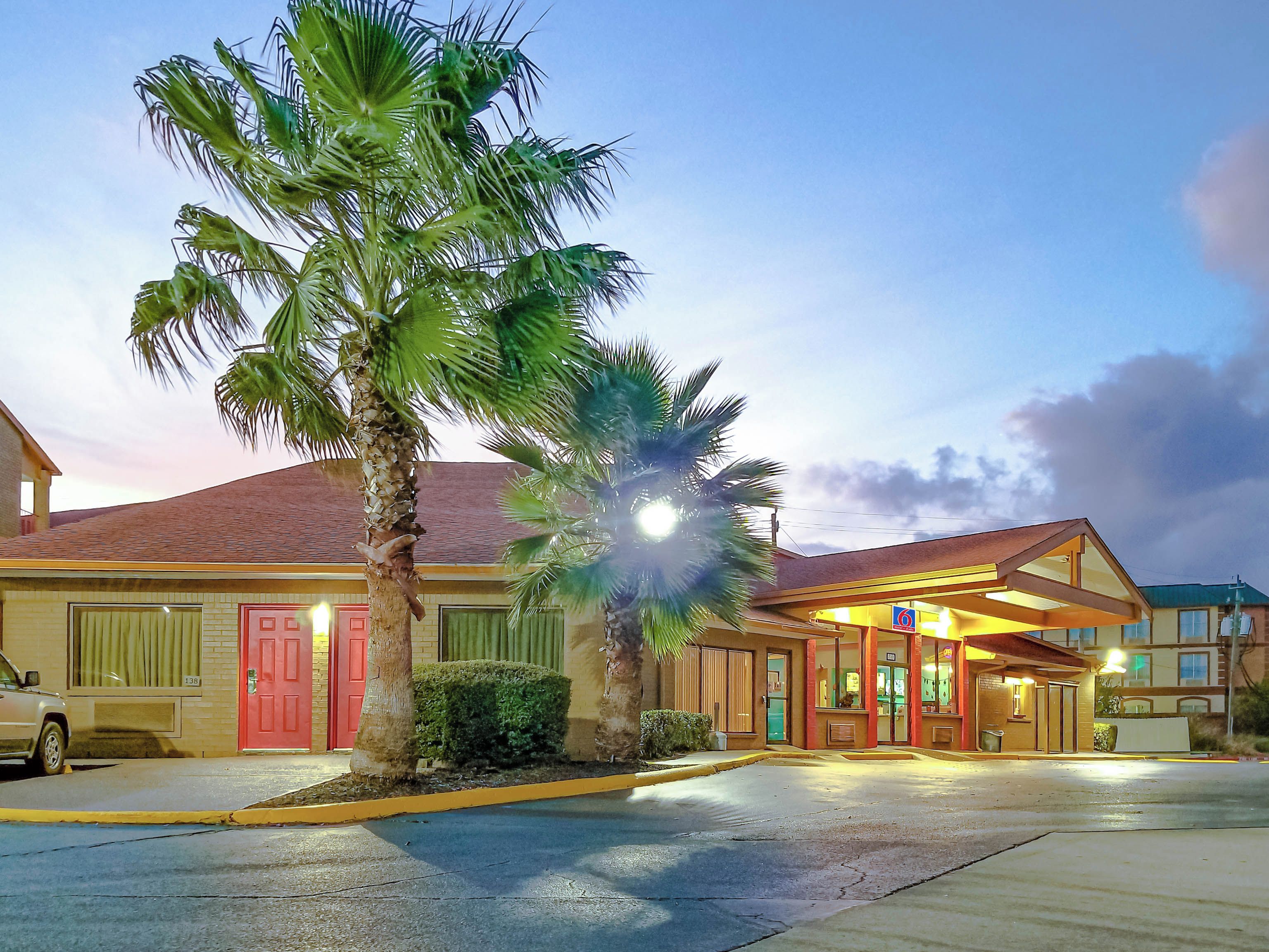 Un hotel con puerta roja, estacionamiento y una palmera.
