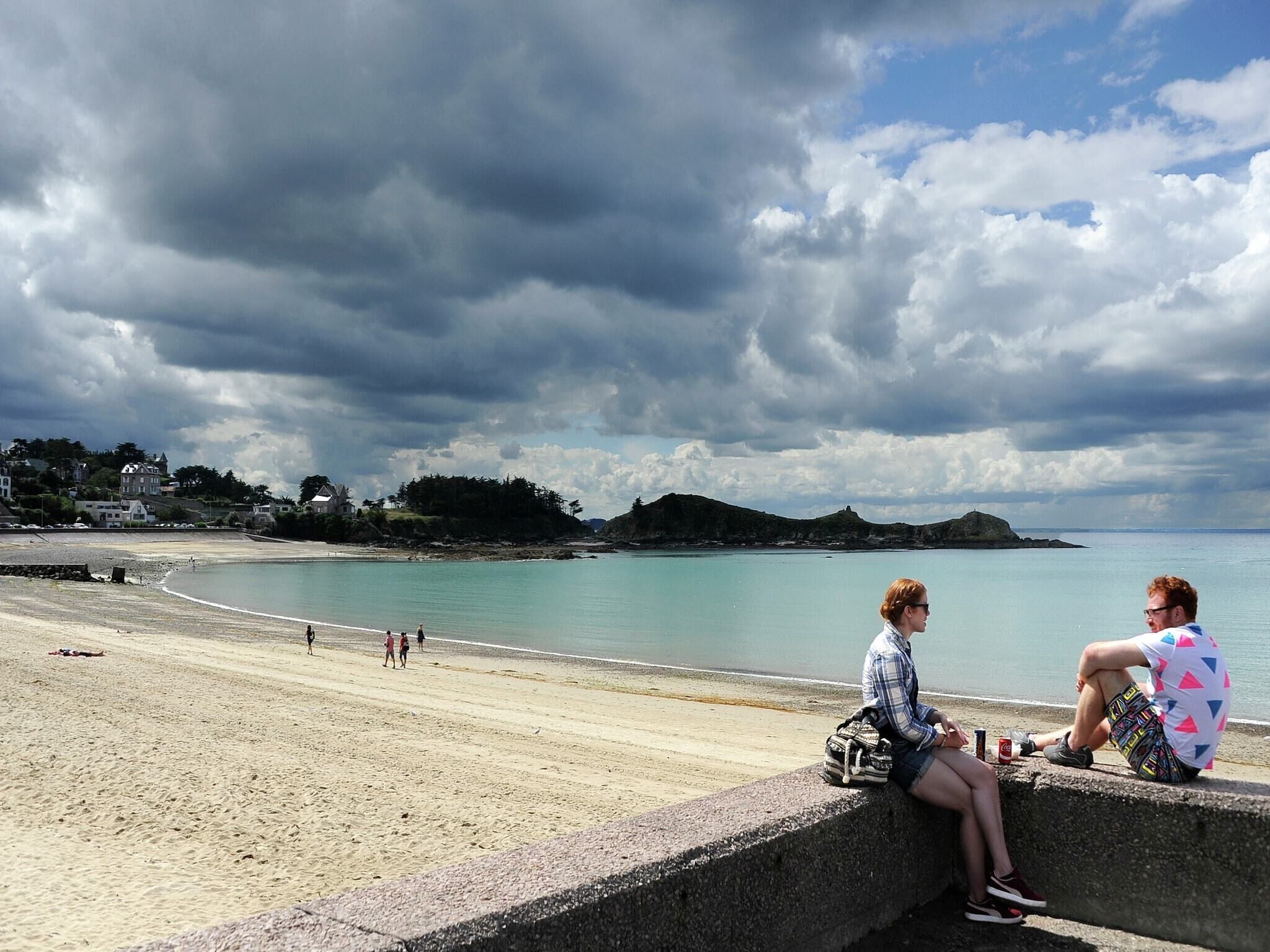 Uma praia com um muro de concreto, mar calmo e céu nublado.