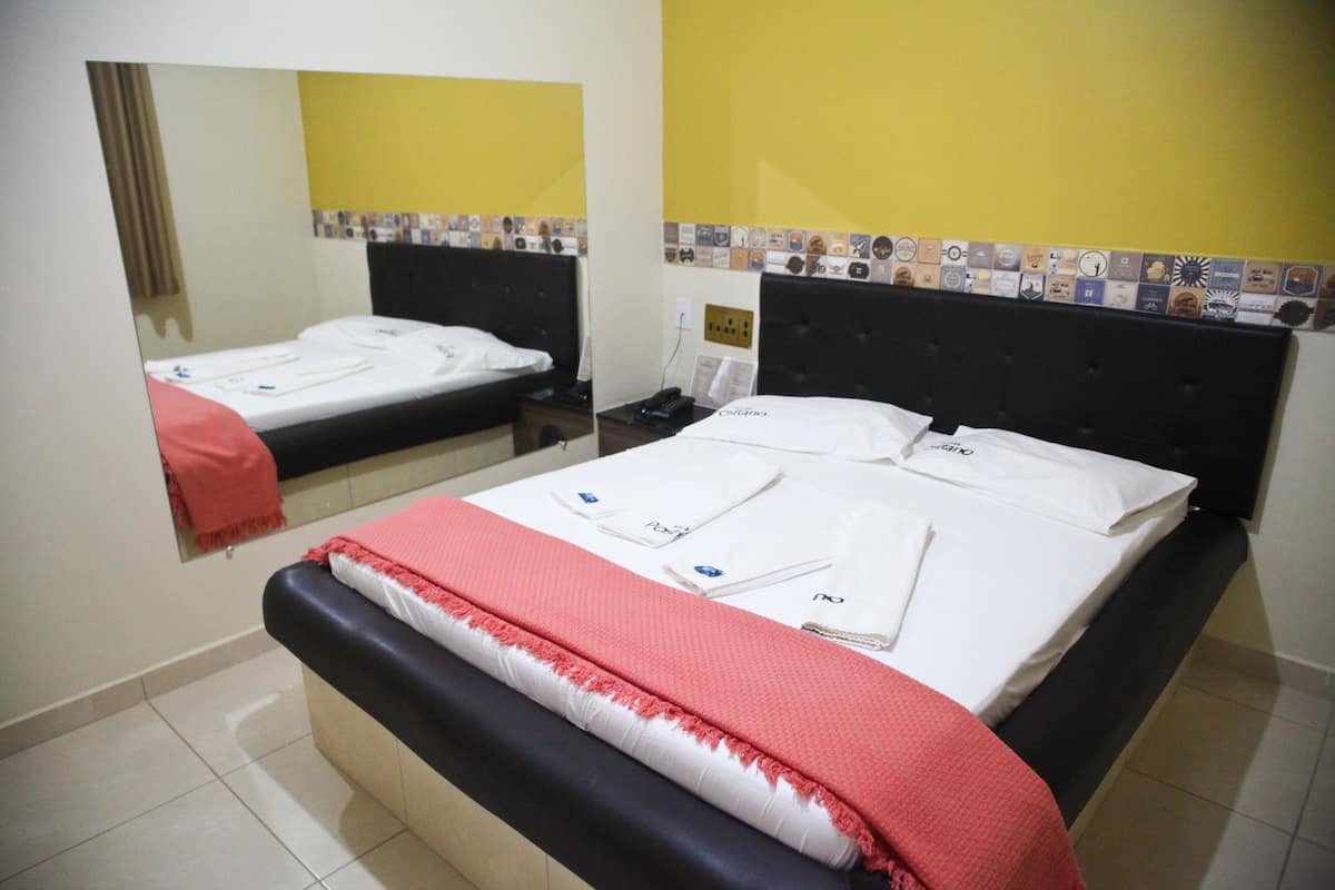 A hotel room with a bed, a bedside table, a mirror, and a wall with a decorative tile border.